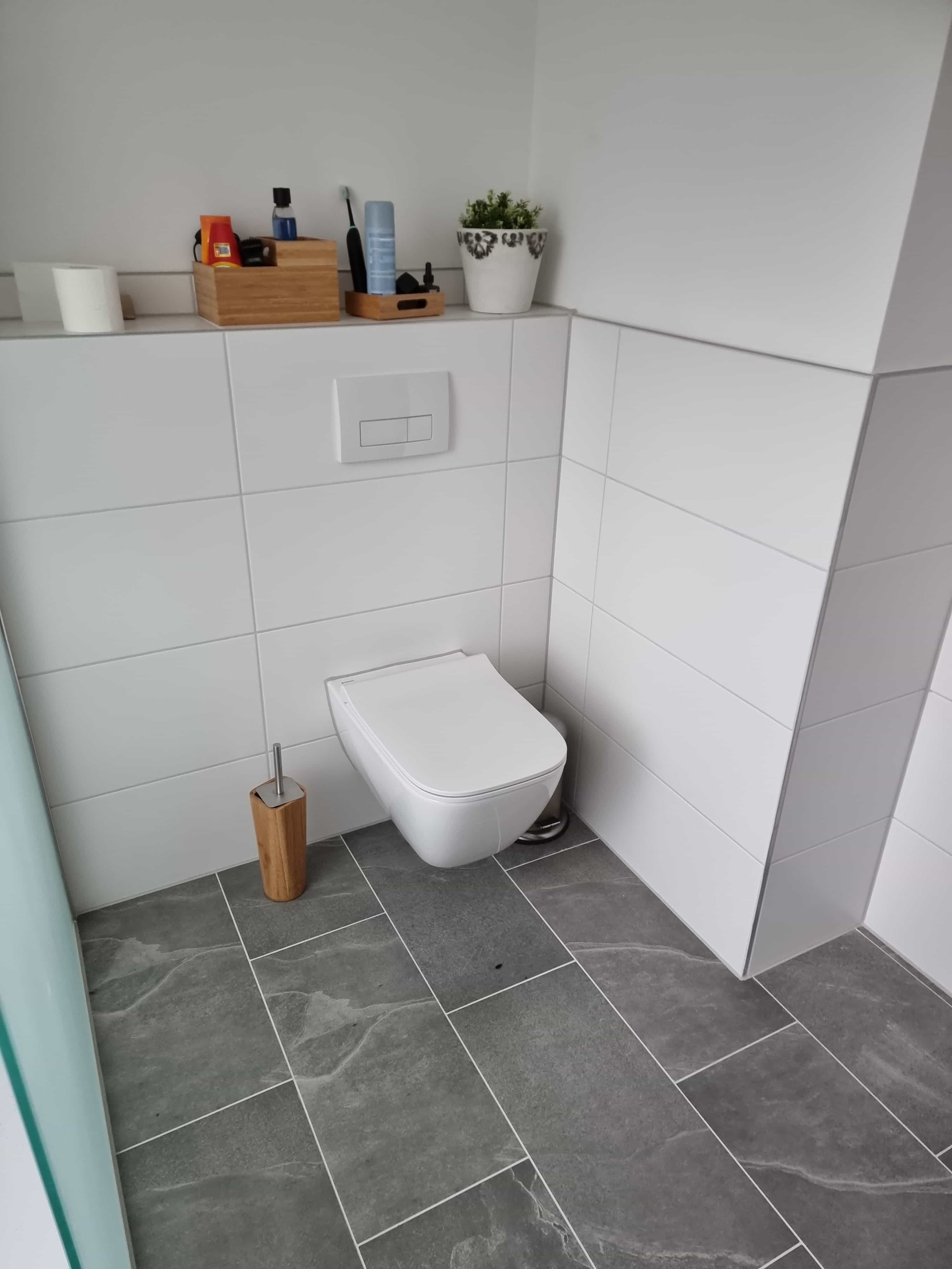 The bathroom was completely renovated by Guido Breitbach. The picture shows a bathroom with a toilet gray floor tiles and white rectangular large tiles on the wall.