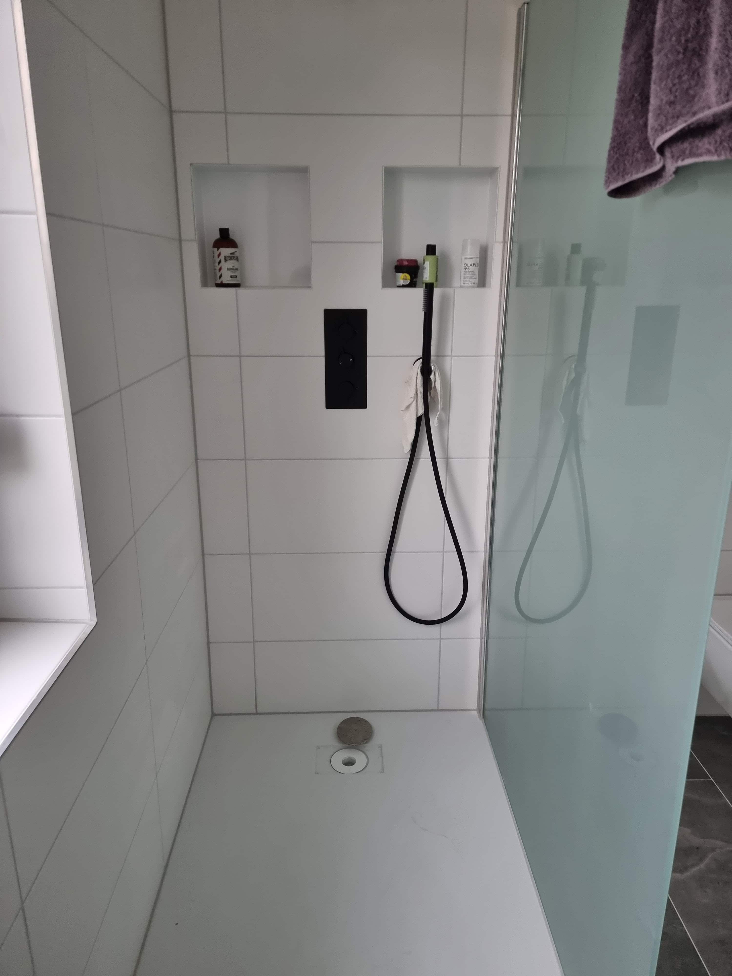 The bathroom was completely renovated by Guido Breitbach. The picture shows a bathroom with a shower and white tiles. Two squares have been incorporated into the wall for shower gel and other bathroom utensils.