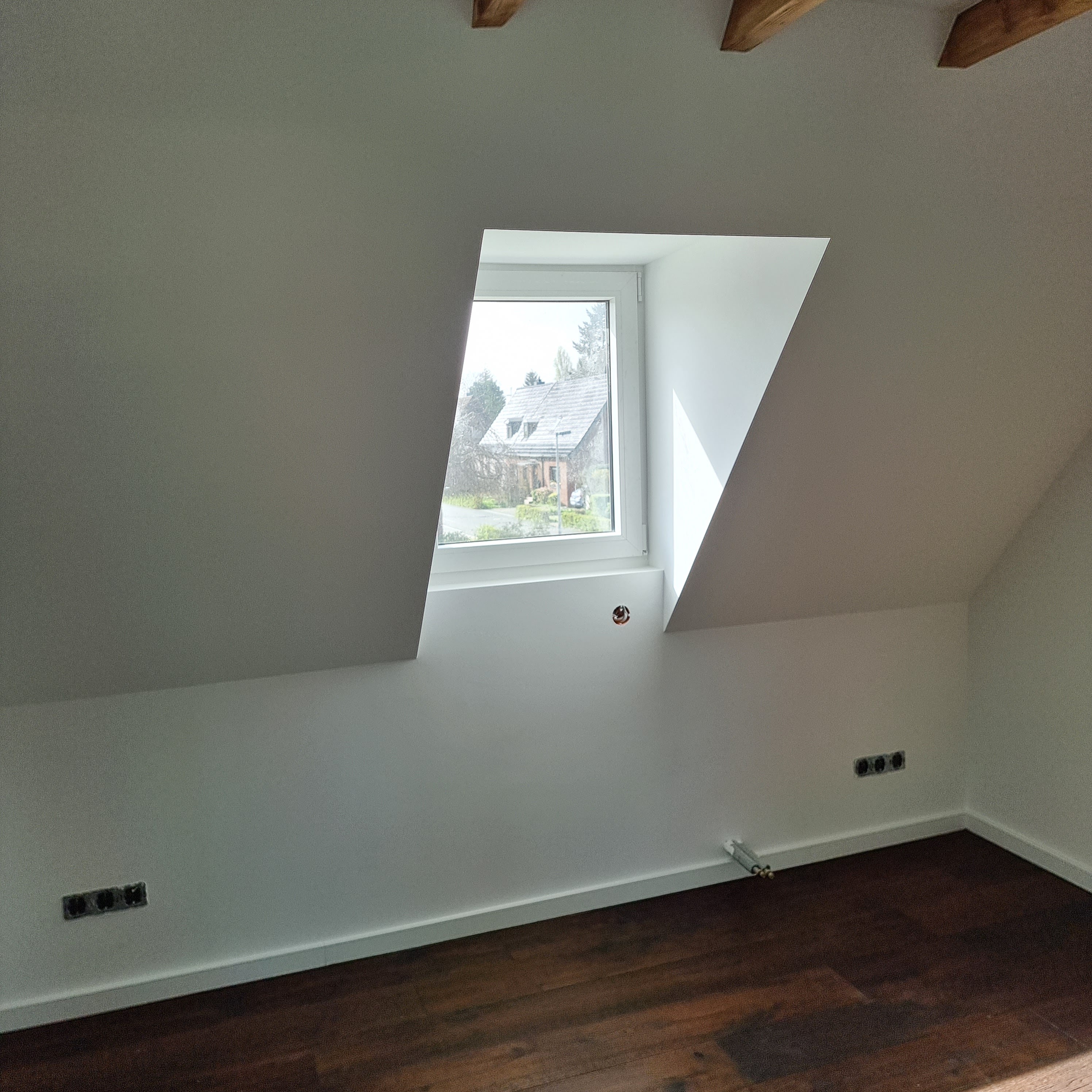 Ein fertig sanierter Dachboden von Guido Breitbach. Der Dachboden hat einen braunen Boden und weiße Wände mit Fenstern.