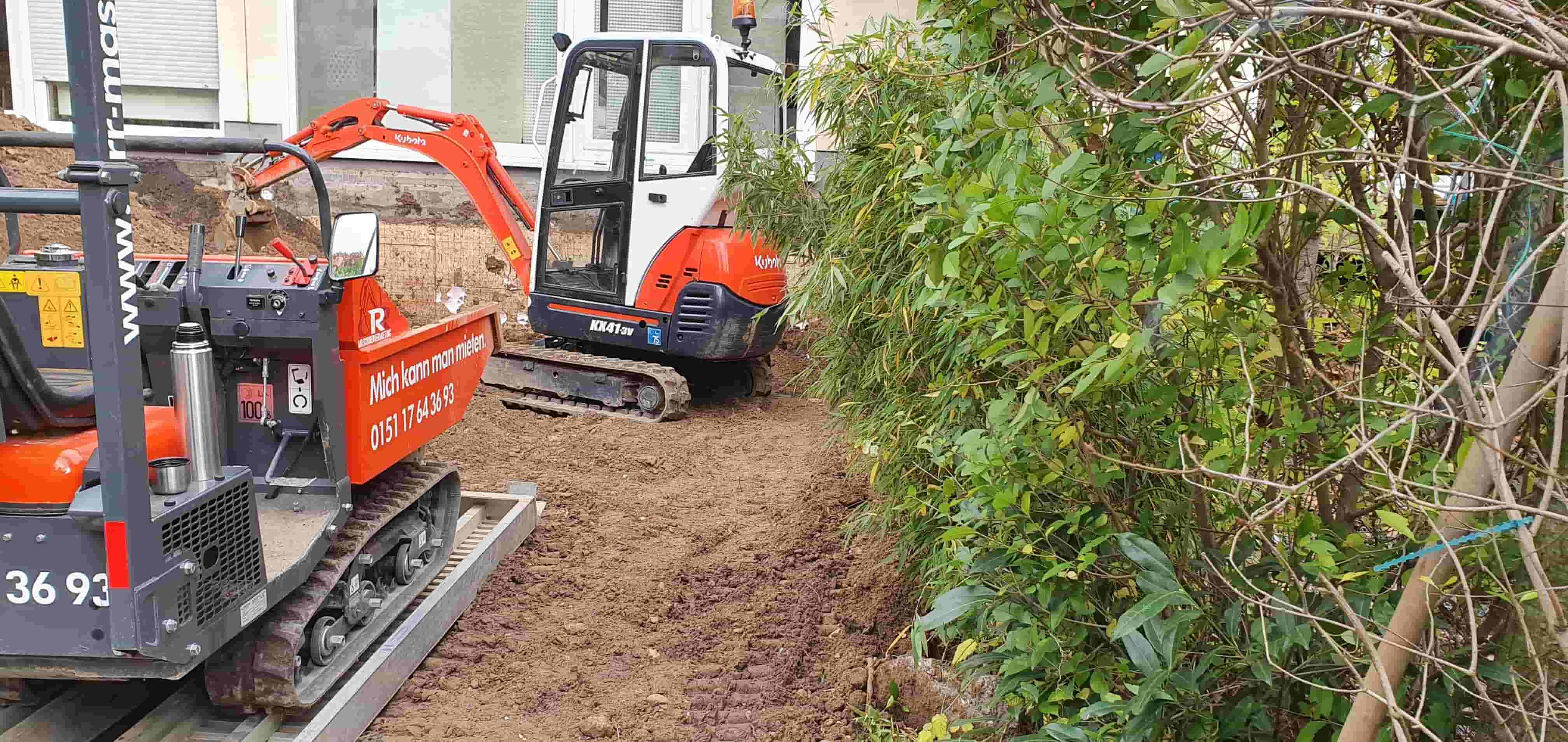 2 Bagger gerade bei der Arbeit. Von Guido Breitbach. Man sieht in der linken Hälfte des Bildes 2 Bagger. Auf der rechten Hälfte des Bildes ist ein Gebüsch zu sehen.